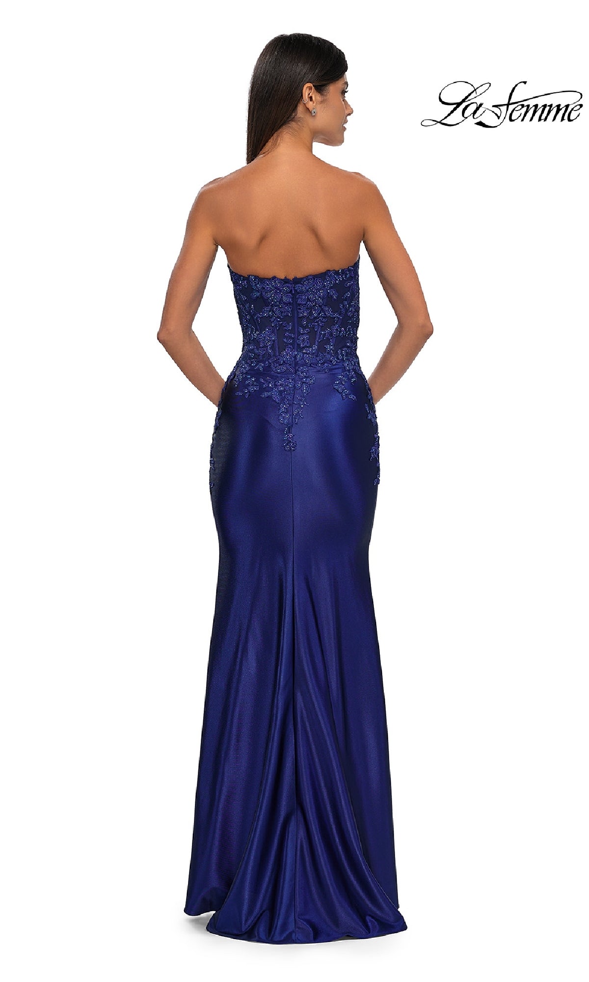 A woman models the Tight Strapless Long Prom Dress La Femme 32582, featuring a fitted royal blue beaded bodice and lace details, shown from the back on a white background with the